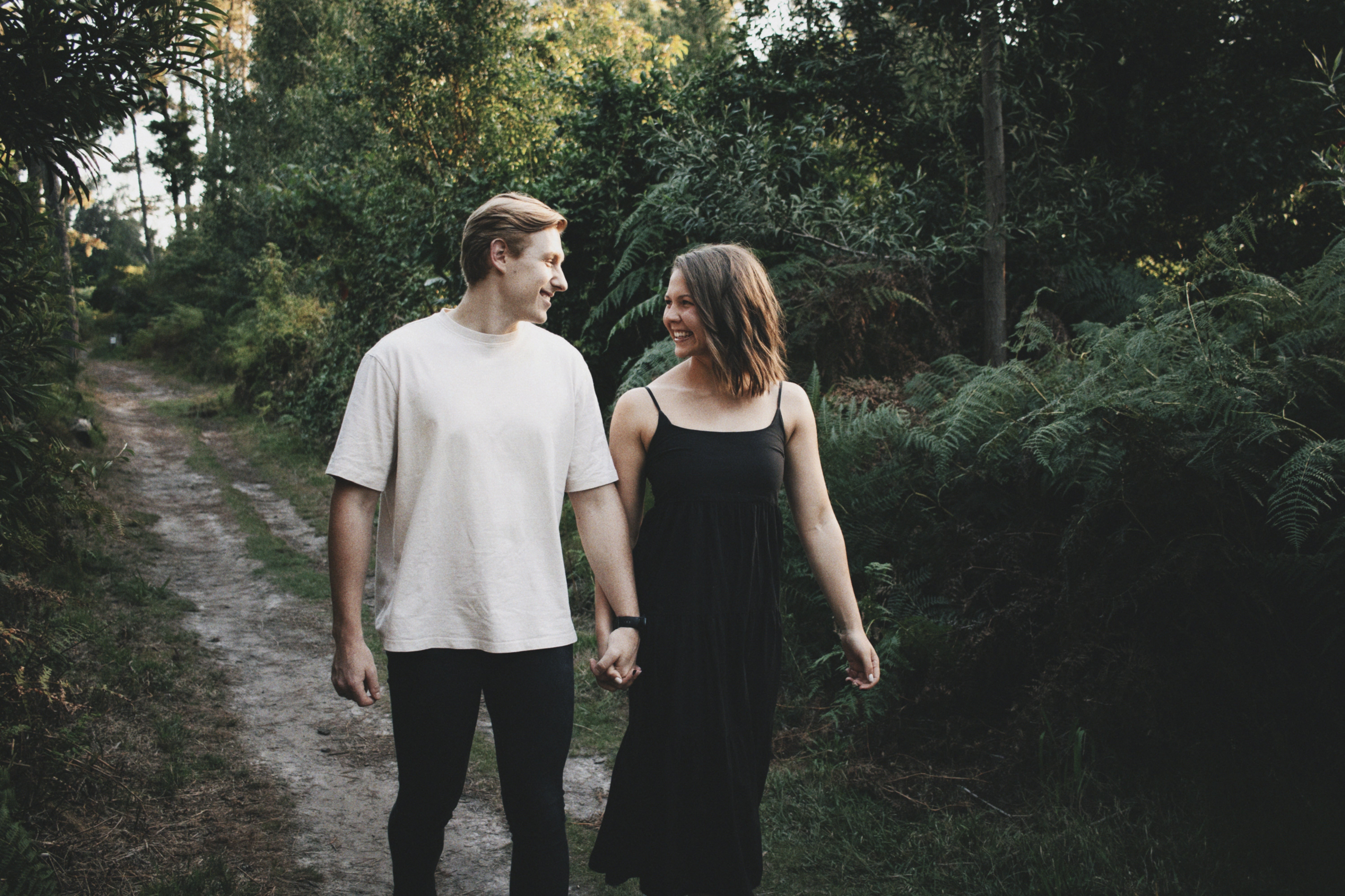 Two people walking hand in hand on a path through a forest.