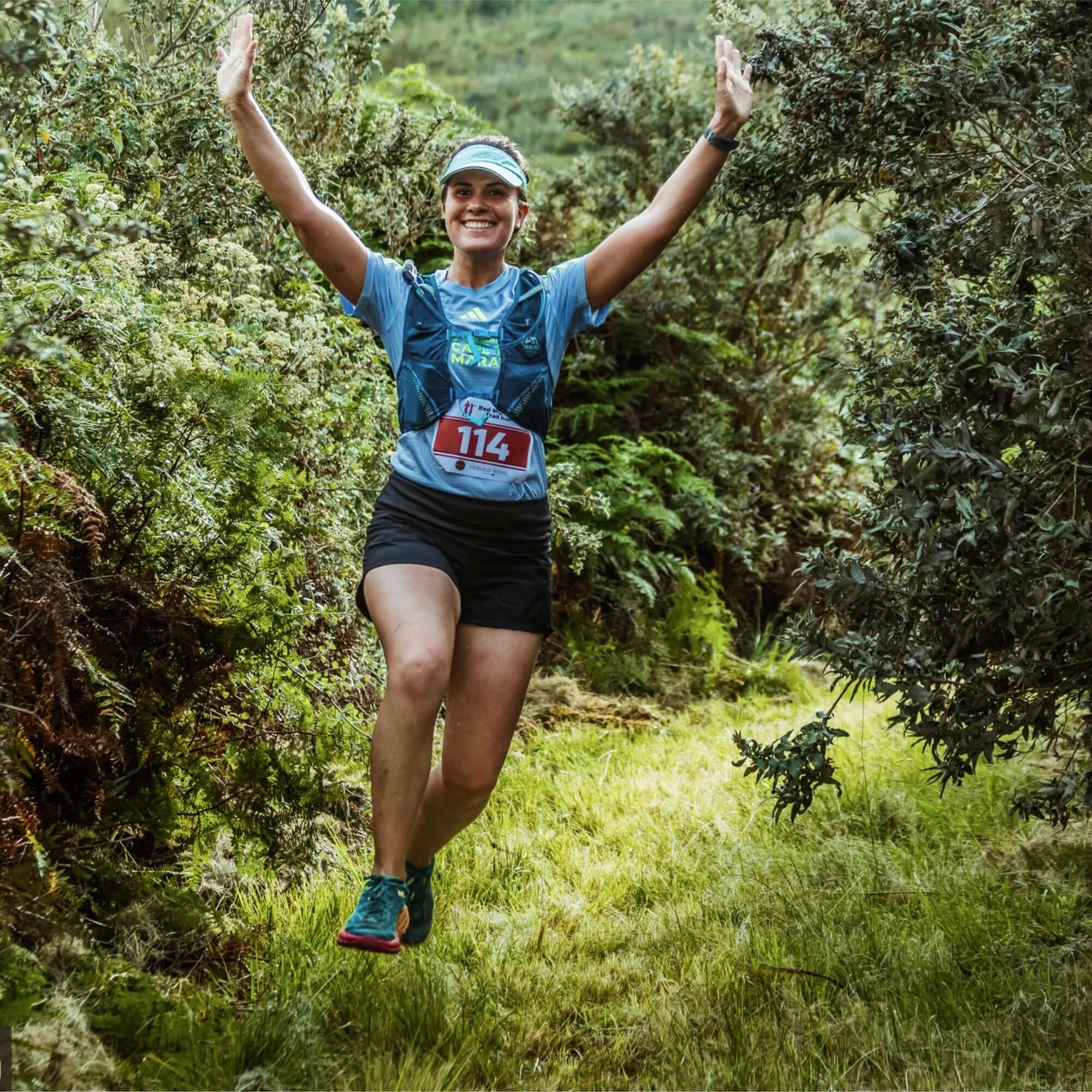 Woman in athletic wear with a race number celebrating in a forest setting