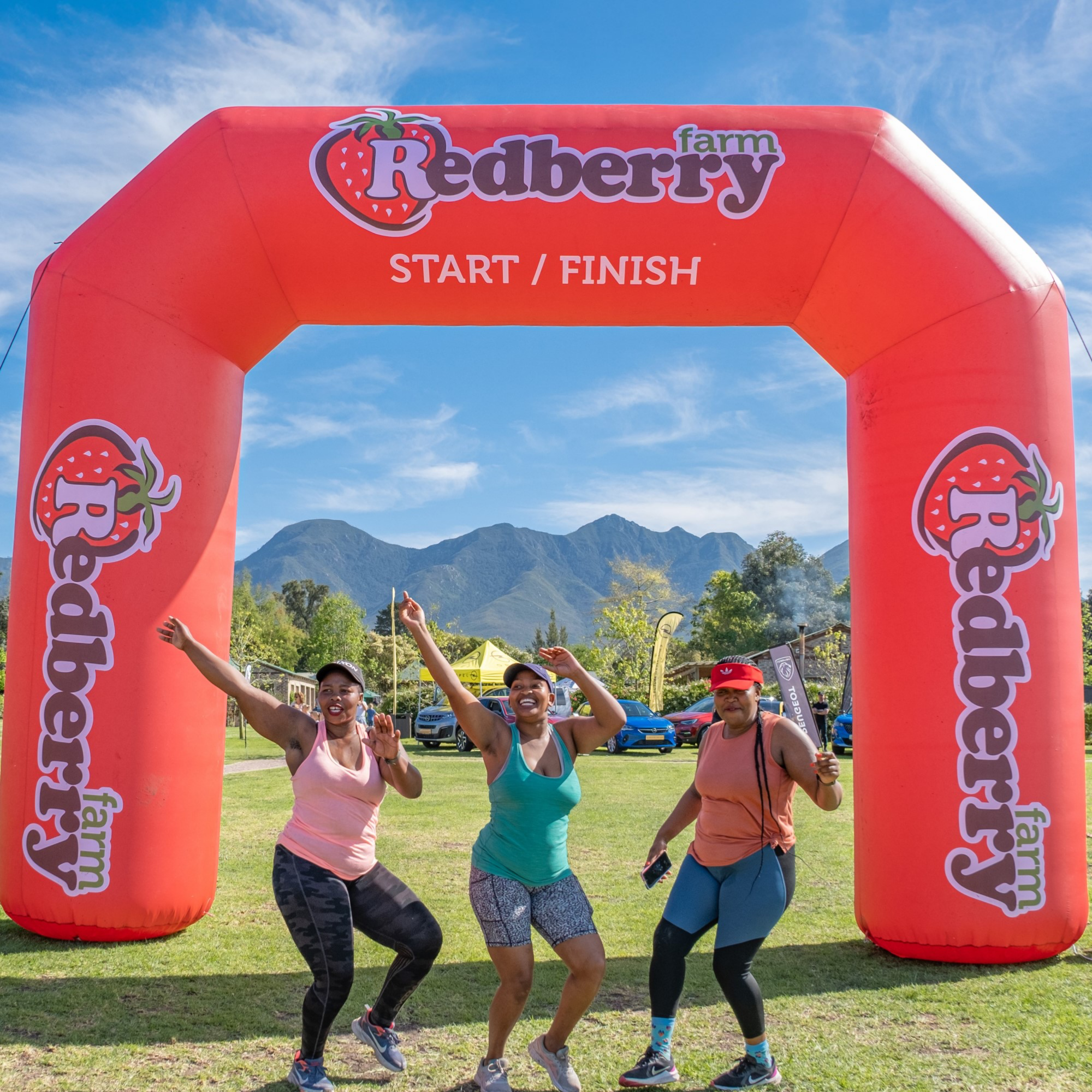 Three women celebrating behind a Redberry Farm inflatable archway with mountains in the background.